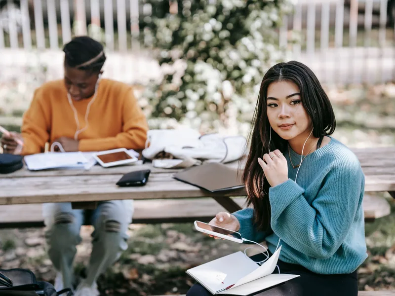 Two students studying together outdoors with notebooks and phones